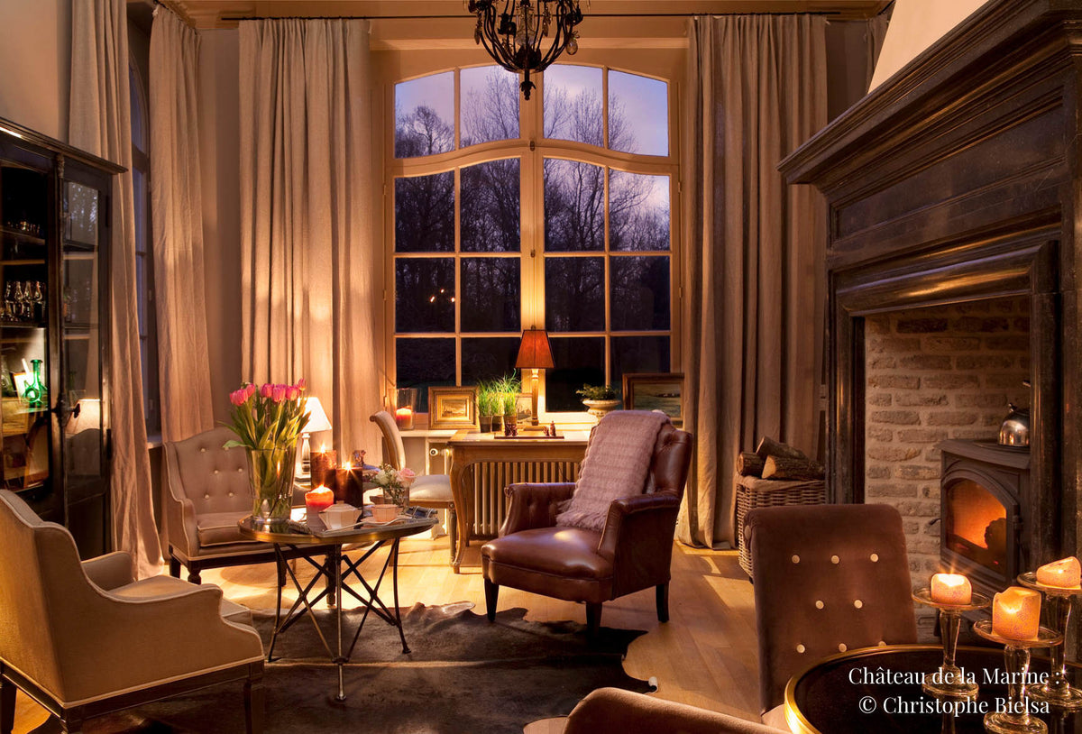 Lobby de château avec une cheminée éclairé par des luminaires et des bougies